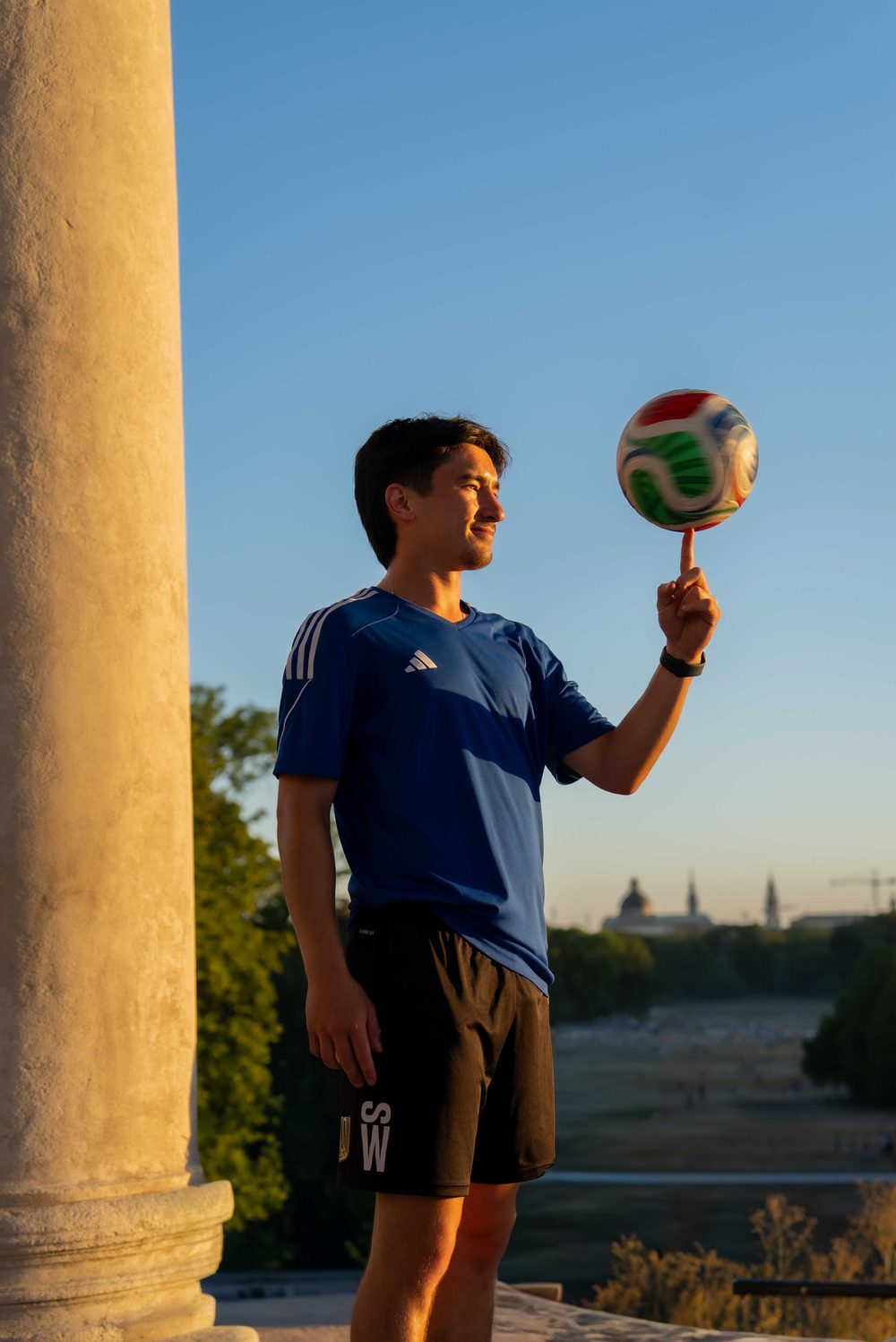 Samuel Weller mit Ball auf dem Finger im Abendlicht, München im Hintergrund